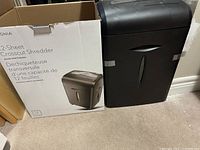 Photo showing the black Insignia crosscut paper shredder next to its original box. The box indicates it can shred up to 12 sheets crosscut at once.