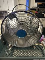 Front view of the small metal fan showing silver cage, blades with blue center.