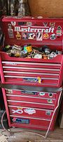 Red Mastercraft metal tool chest and lower cabinet with stickers, several drawers open revealing tools.