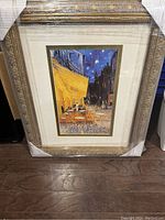 Framed oil painting of a café terrace at night with starry sky, set in an ornate gold frame with corner protectors.