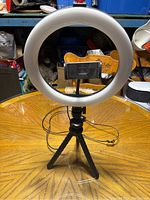 Photo showing circular ring light mounted on tripod with phone holder and USB cable on wooden surface.