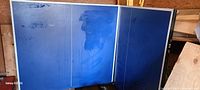 Full view of the ping pong table folded partially, showing playing surface with scuff marks.