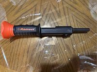 Single Ramset hand tool shown on wooden surface with clear overlay reflecting light. Photo focuses on tool's handle and shaft.