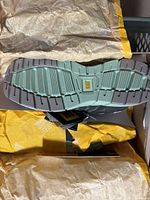 Sole view of single black Cat safety shoe showing light mint green treaded rubber sole with CAT logo.