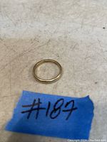Photo of a vintage 10K gold band ring placed on a scratched surface with a blue tape labeled '#187'.