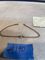 Single 14K gold chain bracelet with central decorative accent displayed with lot tags