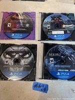 Four PS4 game discs: Batman Arkham Knight, God of War, Darksiders Warmastered Edition, Sekiro Shadows Die Twice.