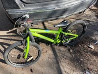 Side perspective of the full green Norco Storm bicycle on concrete near vehicle rear bumper, showing frame, tires, seat, handlebars.
