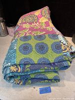 Folded quilted comforter showing patchwork design with mainly blue, green, purple, pink, and beige colors.