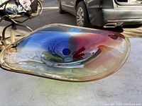 Photo showing angled view of the art glass bowl highlighting its shape and vibrant colors including blue, red, green, and amber shades.