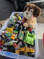 Plastic bin with assorted kids toys including stuffed animals, toy trucks, and action figures