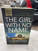 Front cover of 'The Girl With No Name' by Lisa Regan showing title, author, and a rural house image.