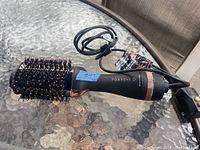 FOXYBAE rose gold hair dryer brush shown lying on a glass surface with visible power cord and control buttons on handle.