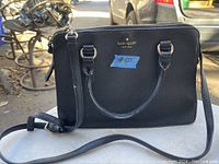 Black leather Kate Spade purse shown from the front with handles and shoulder strap.