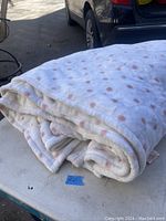 Folded white plush blanket with light pink polka dots visible, showing general appearance and condition.