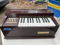 Oblique front view showing overall organ body, keyboard, branded plaque, and control switches.