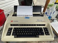 Vintage Olympia Electronic Compact 2 typewriter with beige housing, black keys, and paper loaded in feeder.