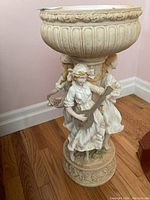 The full bird bath showing the large bowl with ornate rim and the pedestal base with three female figurines holding musical instruments.