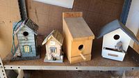 Four wooden bird feeders on shelf, showing variety of designs and materials used