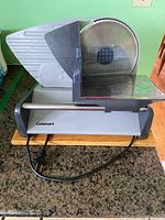 Front view of Cuisinart electric food slicer showing circular blade, body, and power cord on wooden cutting board base.