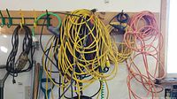 Full view of wall with multiple extension cords hanging coiled on hooks in various colors: yellow, orange, black.