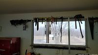 Wide view showing axes, hatchet, levels, and snips mounted on hooks above a window inside a shed