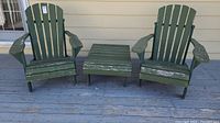 Two green wooden Muskoka chairs and matching side table with weathered and chipped paint, displayed on wooden deck.
