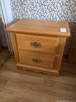 Front view of the solid oak nightstand showing two drawers with ornate metal pulls and natural wood finish.