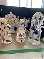 Four blue and white porcelain figurines including a carriage clock with horses and driver, a man playing a violin with a dog, a woman with a dog, and a man in period dress.
