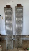 Two galvanized metal ramps leaning against a wall showing length and general condition with rust spots and wear visible.