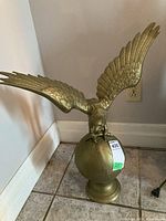 Full view of the metal eagle sculpture with wings spread and perched on a spherical base against corner wall.