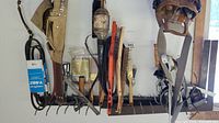 Overview of tool belts, wire brushes, screwdrivers, and measuring squares hanging on the wall