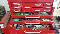 Photo showing red toolbox drawers partially open revealing various hand tools scattered inside drawers.