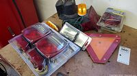 Lot of trailer lights and accessories including tail lights, a warning triangle, and a yellow warning light on a workbench.