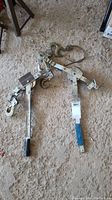 Two metal come-along hand winches laid on a rough floor surface, showing overall build and components including hooks and lever handles.