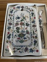 Floral patterned ceramic cheese board in its box with a matching cutter next to it.