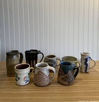 Full view of all eight Doe Ridge stoneware mugs showing varying styles, colors, and designs.