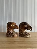 Front view of two handcrafted carved wooden eagle head bookends, showing detailed feather and beak carving in brown wood