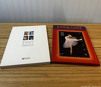 Photo of two vintage U.S. stamp books from 1997 and 1998 placed on a wooden table.