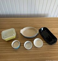 Yellow square covered container, blue ramekin, white ramekins, beige oval dish with blue rim, black rectangular tray