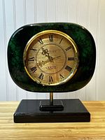Front view of vintage green silver leaf quartz clock with Roman numerals on gold-toned dial, mounted on black base.
