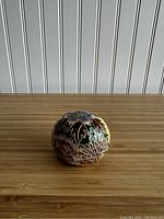 Photo of spherical cloisonné enamel paperweight with gilded floral details on a wooden surface, showing multiple angles