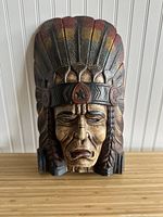 Front view of the carved Native American chief bust with painted headdress and facial features