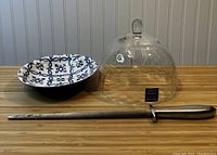 Front view showing the ceramic bowl with blue and white pattern, clear glass lid, and metal cutter tool on wooden surface.