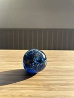 Vintage Murano blue glass paperweight shown from an angle with sunlit confetti-like interior details visible inside.