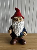 Front view of vintage porcelain standing gnome figurine with red hat, blue shirt, brown pants, holding walking stick.