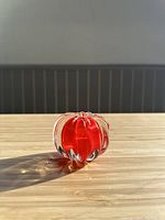 Front view of the red and clear Murano glass paperweight showing its vibrant color and form on a wood surface with gray wall background.