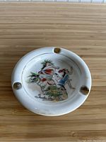 Top view of ashtray showing colorful 'Honi Honi Dancers' illustration and three cigarette rests around rim