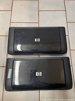 Two HP OfficeJet H470 mobile printers closed, top view showing HP logo on lids, black plastic body with minor scratches.