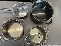 Four assorted pans and saucepans viewed from above, showing lids and handles.